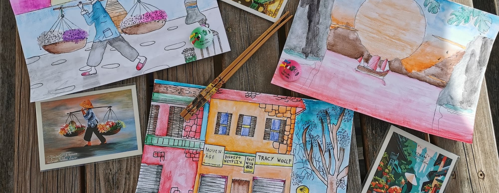 Dessins et cartes postales à l'aquarelle étalés sur une table en bois