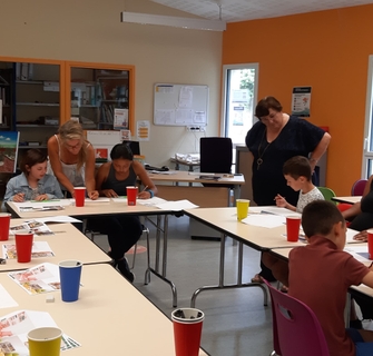 Cours de dessin enfants : l'intervenante guide deux enfants à table