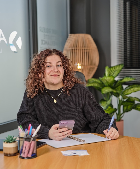 Portrait de Clothilde, assistante administrative indépendante, assise à son bureau avec son téléphone et son carnet