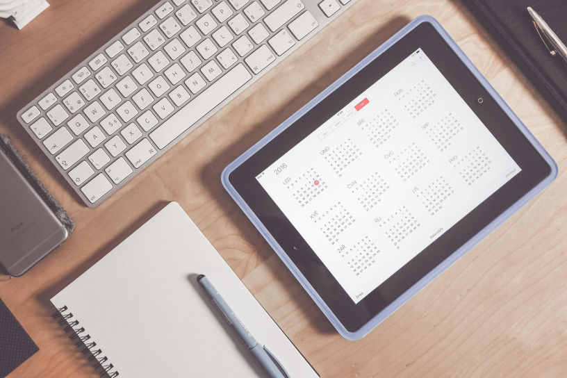 Tablette affichant un calendrier posée sur un bureau à côté d'un clavier et d'un carnet