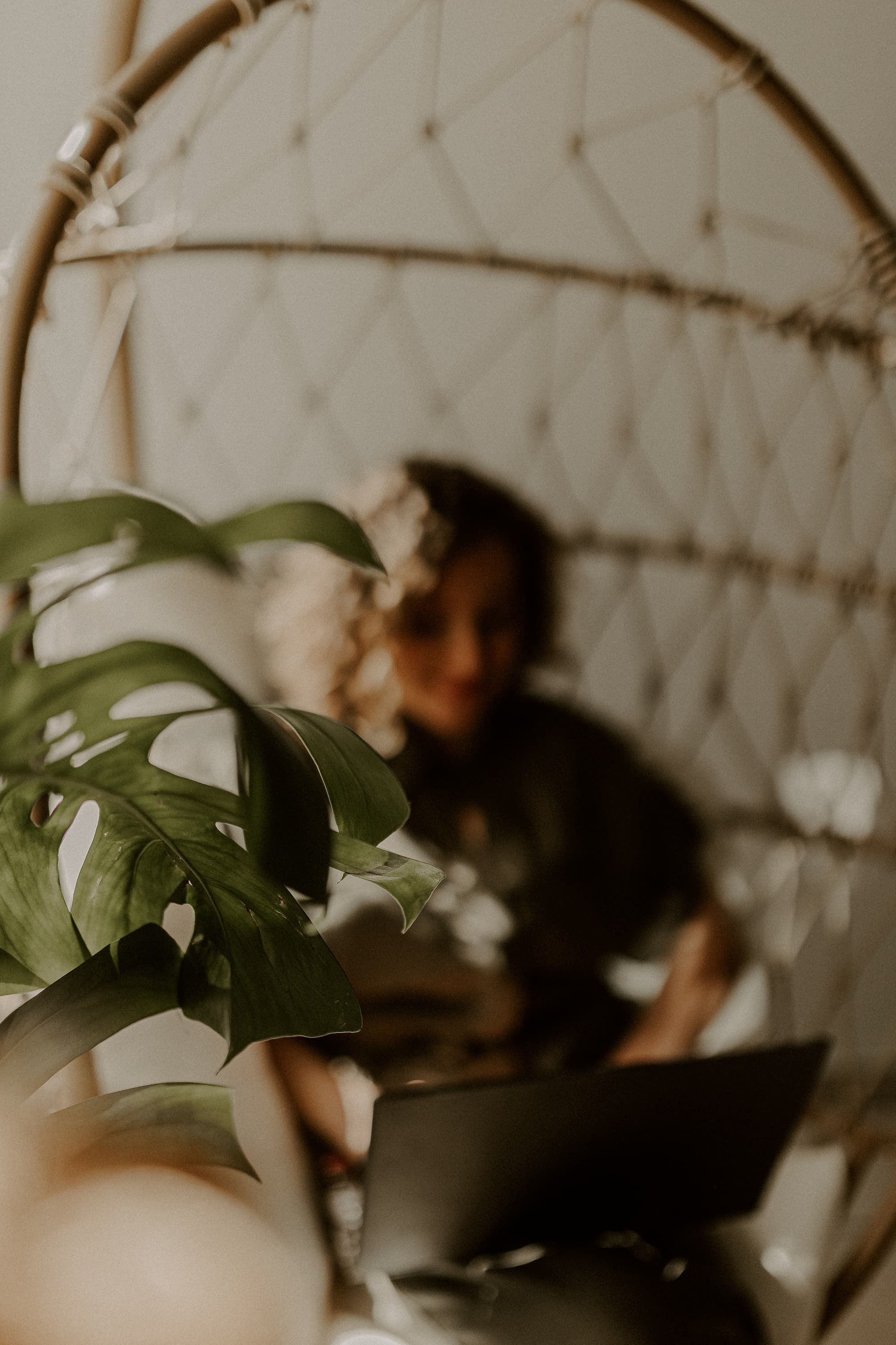 Clothilde assise dans un fauteuil suspendu avec son ordinateur portable, en arrière-plan flou derrière une plante