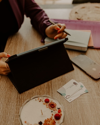Clothilde travaillant sur sa tablette à son bureau, carnet et cartes de visite CloAssist' posés sur la table