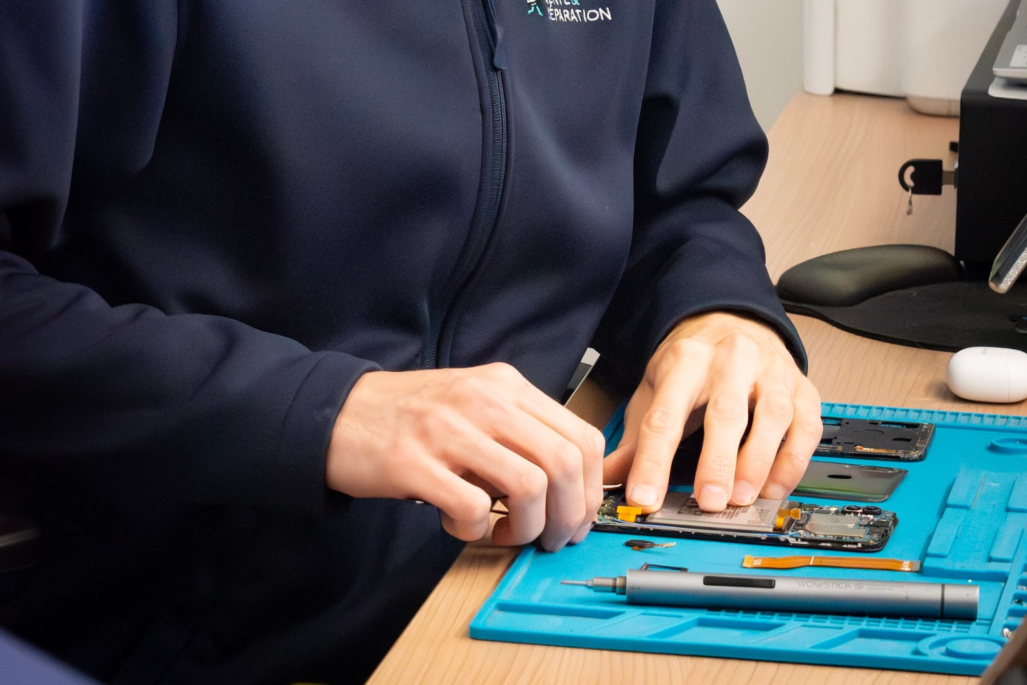 Mains de Yohan réparant un smartphone sur le tapis de l'atelier Phone Occaz