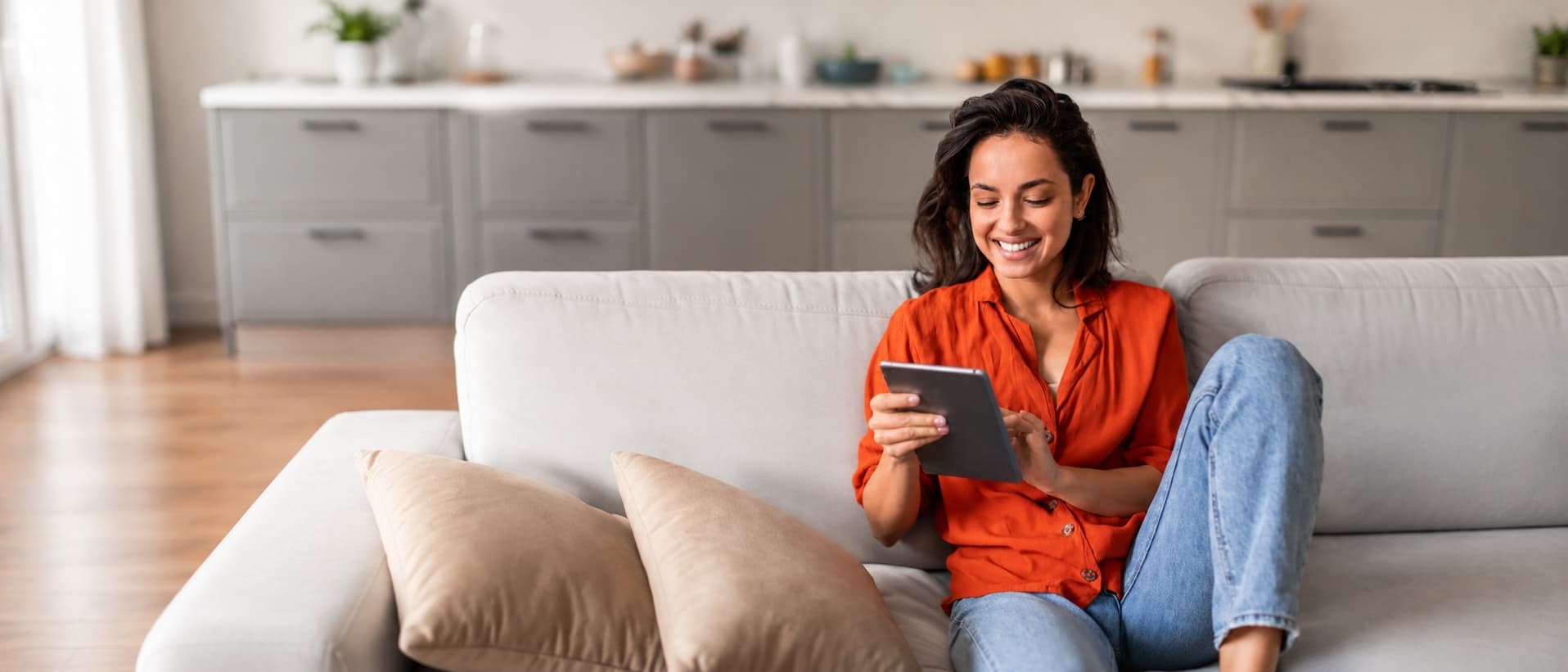 Femme souriante lisant un article sur sa tablette dans son salon