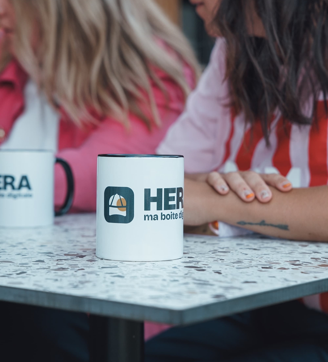 Gros plan sur des tasses Hera, membres du collectif en arrière-plan