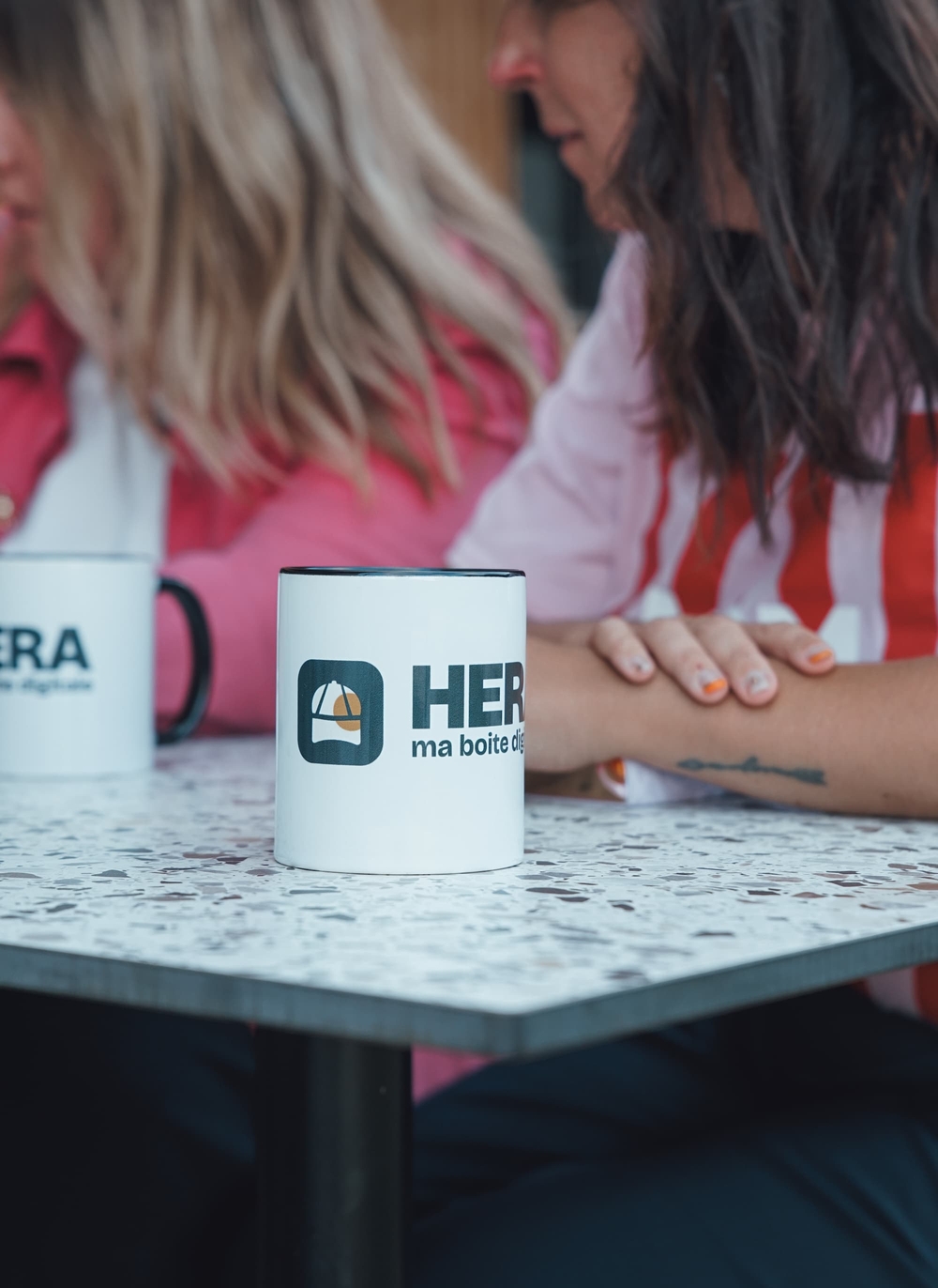Gros plan sur des tasses Hera, membres du collectif en arrière-plan