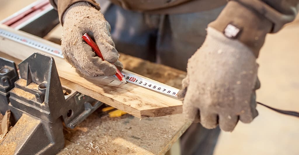 Mains d'un charpentier prenant des mesures sur une planche de bois