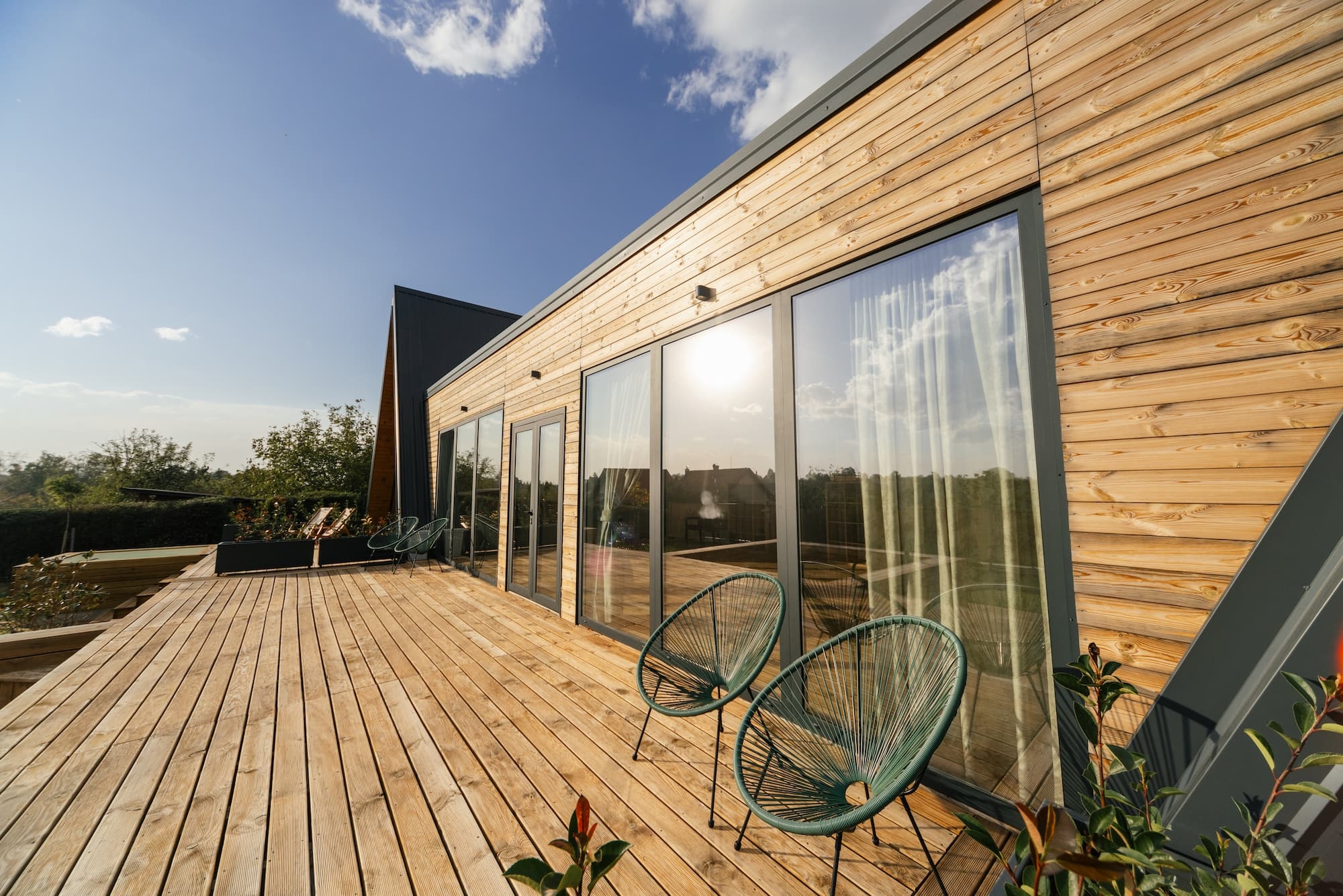 Terrasse en bois le long d'une façade à bardage bois et grandes baies vitrées