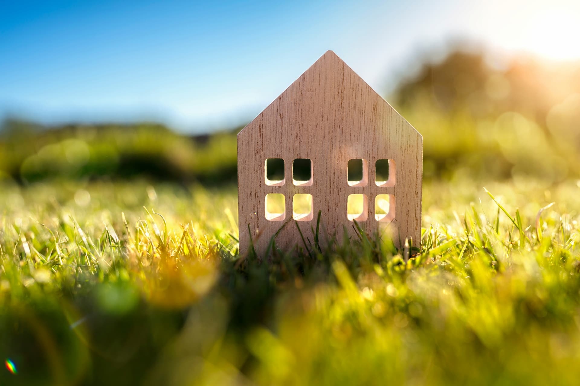 Petite maquette d'une maison en bois posée dans l'herbe au soleil