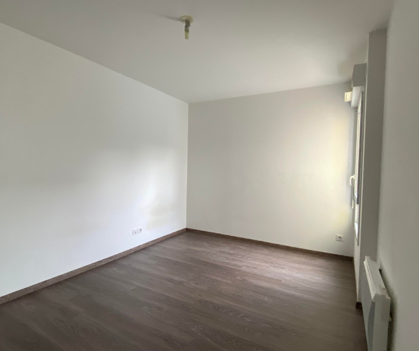 Chambre vide avec murs blancs, parquet foncé, lumière naturelle grâce à baie vitrée avant home staging à Nantes