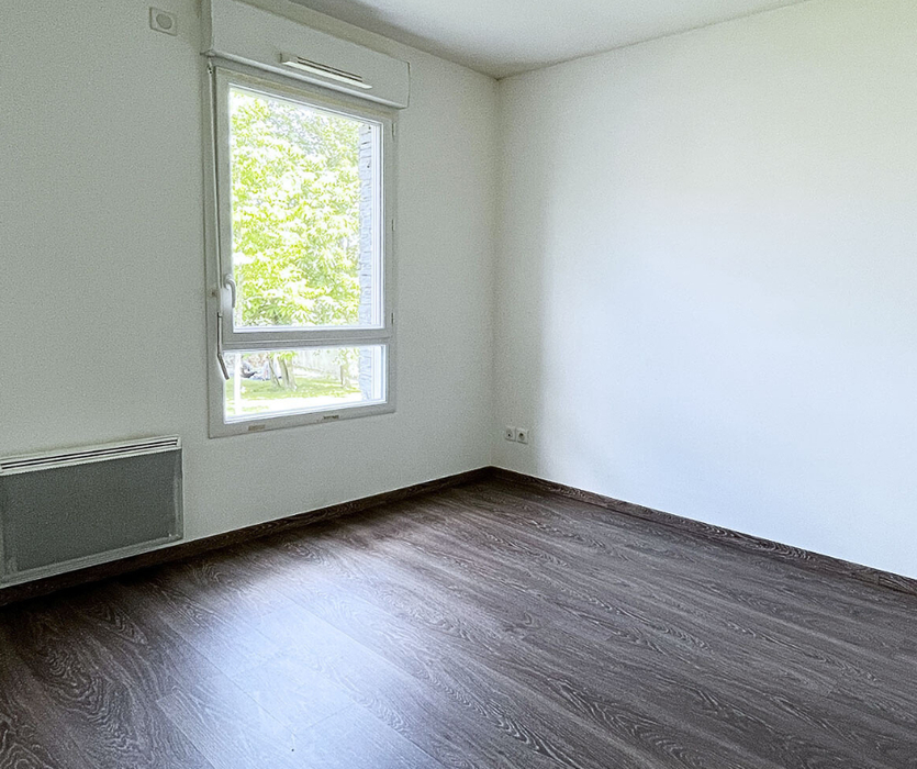 Petite chambre pouvant convenir à une enfant, vide avec murs blancs, parquet foncé et fenêtre donnant sur la végétation avant home staging à Nantes