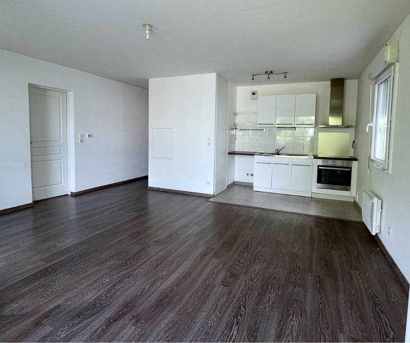Espaces vides avant mise en valeur  à Nantes : parquet foncé uniforme, murs blancs, lumière naturelle traversant l’appartement, cuisine blanche et fonctionnelle.