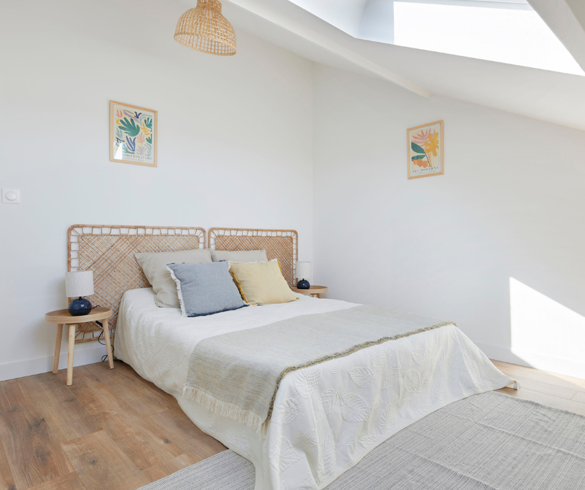chambre parentale installée dans pièce sous comble avec lit jeté de lit coussins tables et lampes de chevet cadres 