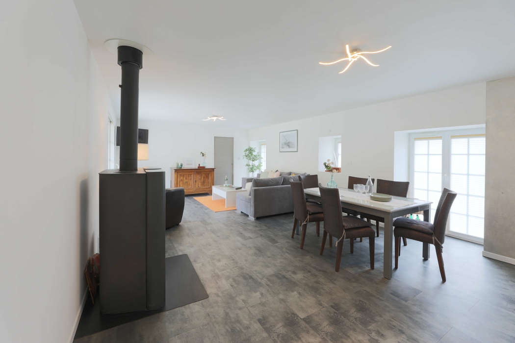 Pièce de vie lumineuse, rangée, épurée avec poele, coin repas avec table chaises, coin salon avec canapé meuble bois après home staging en bretagne