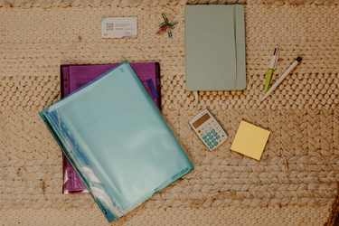 Pochettes, carnet, calculatrice et cartes de visite CloAssist' posés sur un tapis tressé