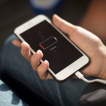 Main tenant un iPhone en charge dont l'écran affiche une batterie presque vide