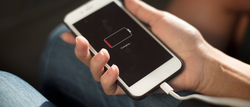 Main tenant un iPhone en charge dont l'écran affiche une batterie presque vide