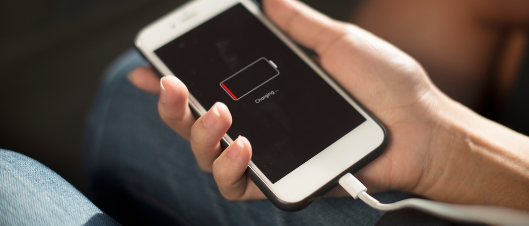 Main tenant un iPhone en charge dont l'écran affiche une batterie presque vide