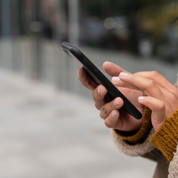 Mains d'une personne en manteau tapant sur l'écran d'un smartphone noir, en extérieur