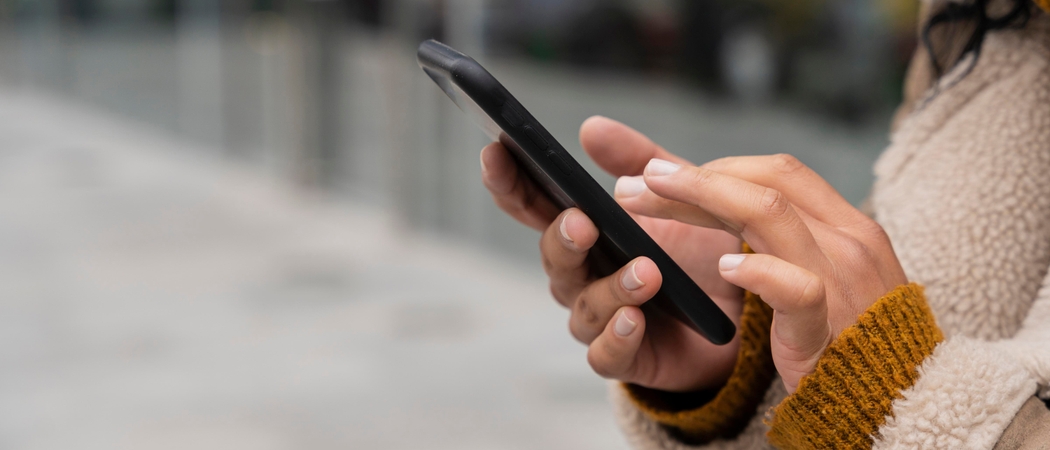 Mains d'une personne en manteau tapant sur l'écran d'un smartphone noir, en extérieur